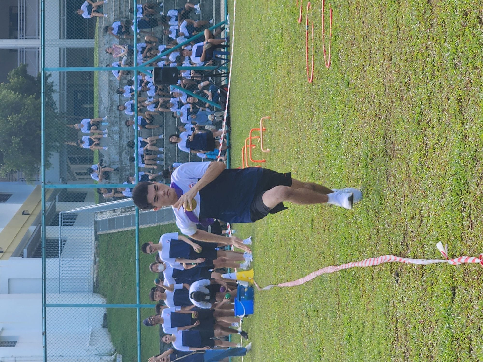 A young male student runs on a grass field holding a ball during an outdoor school sports day event.